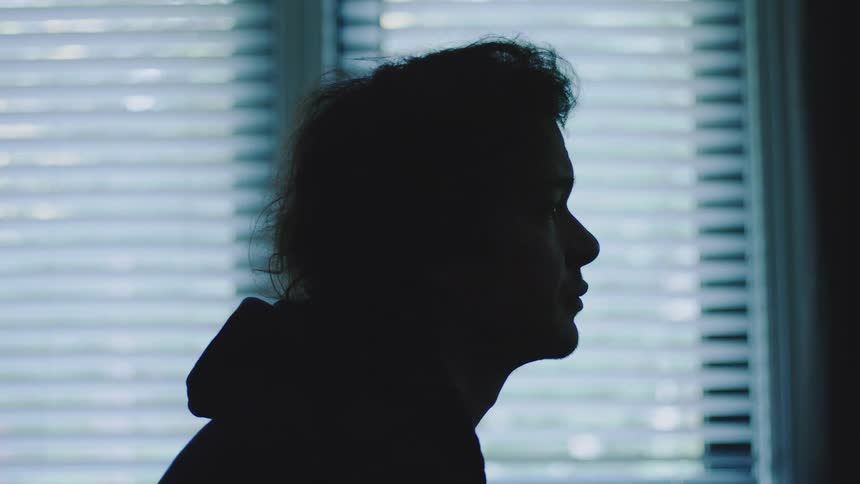 Silhouette of a male person sitting down next to a window in a room indoors during day time