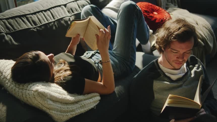 A young man sits beside the window reading a book at midday
