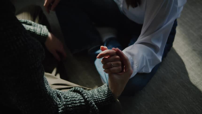 Man and a woman sitting cross legged on the floor hold hands