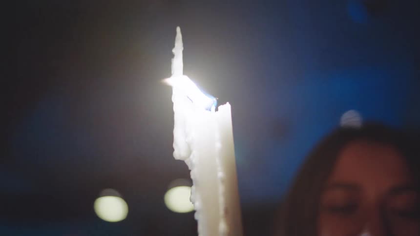 Close up of a young woman standing beside a lit candle in a dark room