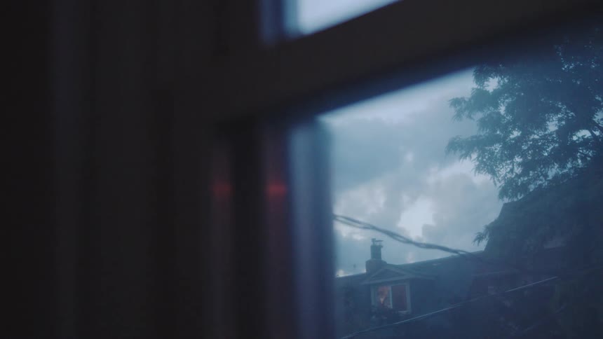 A cloudy sky is seen through the window with a tree beside another building at midday