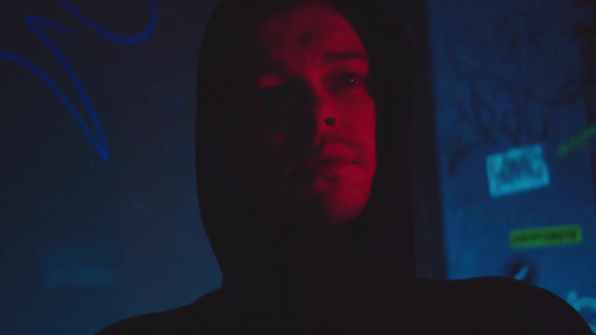 Young adult man wearing a black hoodie standing near the wall on a club indoors during night time