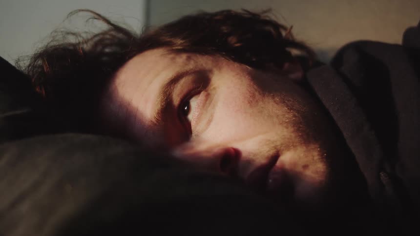 A man laying in bed slowly opens his eyes and looks up at sunlight