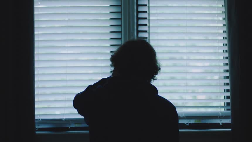 The man looks out the window in the dark room