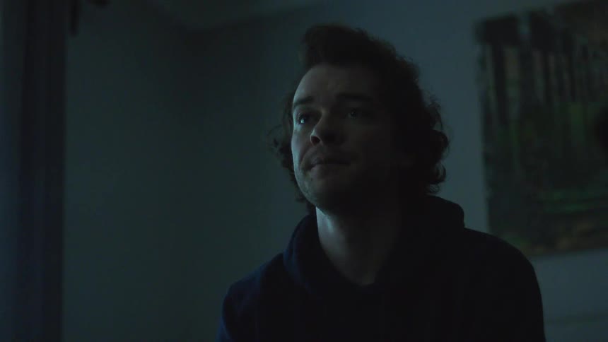 Man seated indoors under low lighting with his gaze directed downward
