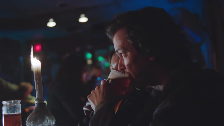 Young couple in bar at night sharing drink cuddled up excitedly in discussion
