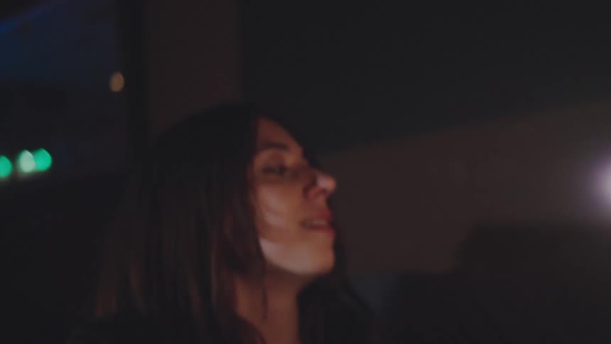 A couple in a dimly lit bar with a single candle on their table laughs embraces and raises their mugs for a toast before drinking their beer