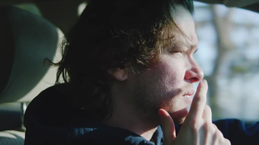 Man with hand on face looking out window in daylightlit car