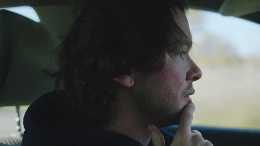 Young adult man driving a car with a nervous facial expression during day time