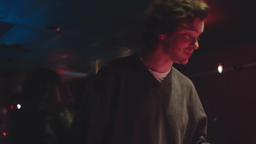 A smiling man and a woman in a leather jacket play pool at a dimly lit bar with neon lights and a dramatic atmosphere