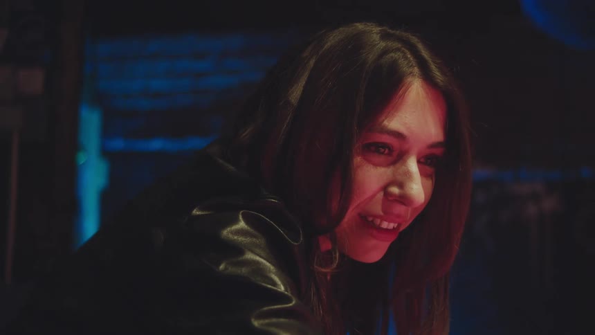 Young adult woman smiling and talking while leaning over a pool table and taking a shot at a ball next to a young adult man watching her move at a pub indoors during night time