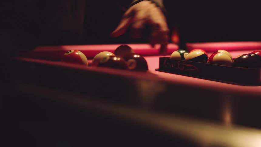 Human hands picking pool balls and putting over a pool table while another set of hands adjust them for the game indoors during night time