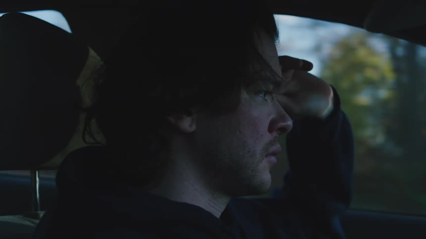 Person in dark hoodie with hand on forehead looking out car