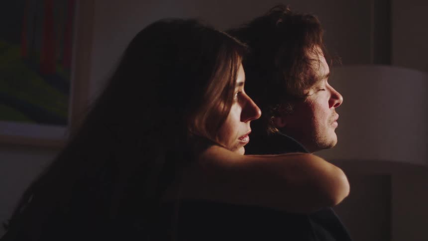 The woman is leaning on the back of the man and they are both looking straight a head like they are deep in thought