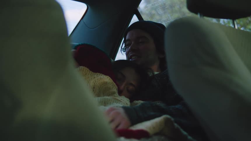 Couple sitting together in car backseat with blanket in dim setting and window in background