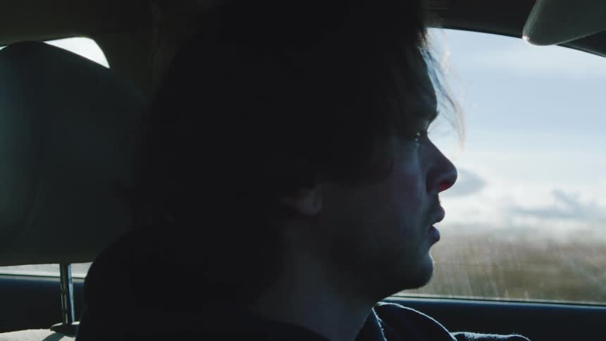 A young man drives his car through the countryside at midday