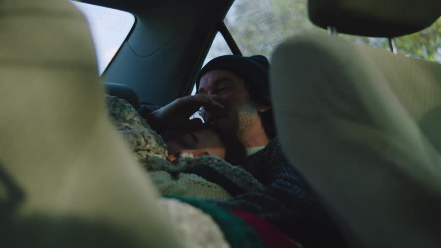 Couple sleeping in the back seat of a car covered with blankets