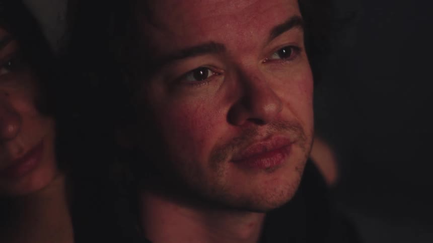 A man and a woman are captured in a very dim closeup shot sharing an intimate quiet moment with gentle light illuminating their faces from the side