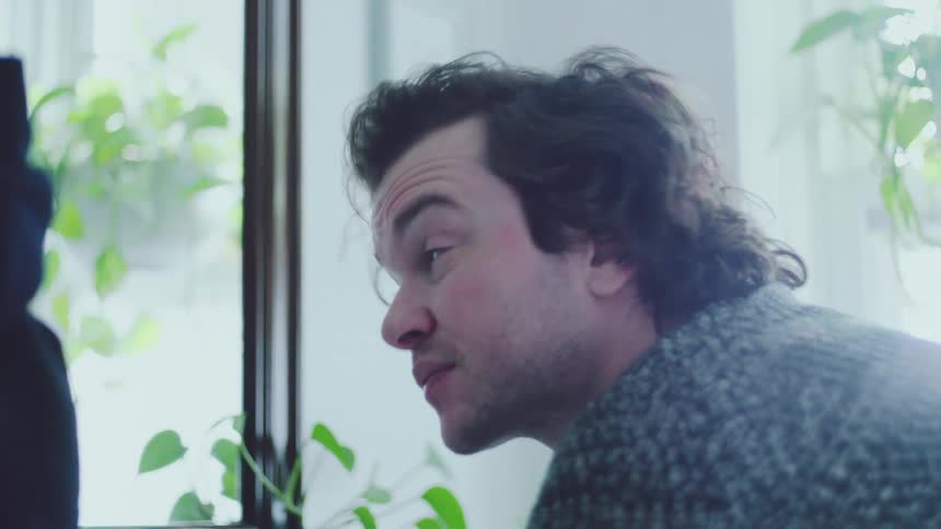 Man leaning near a mirror looks toward the window then towards another person