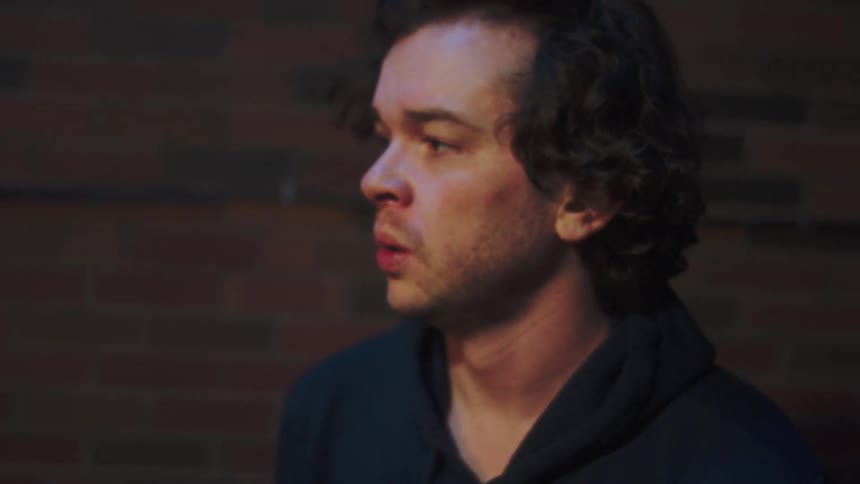 Young adult man wearing a black hoodie looking around with a scared facial expression on an alley outdoors during night time