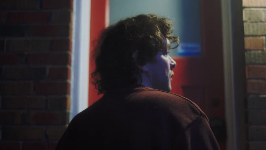 A young man knocks on a red door as an older male opens it with excitement at night