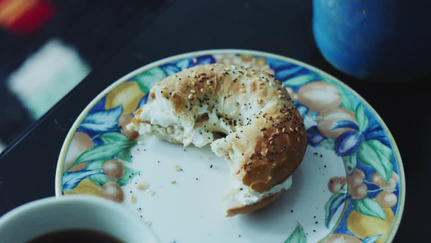 A seeded bagel with cream cheese and a bite taken out rests on a patterned plate