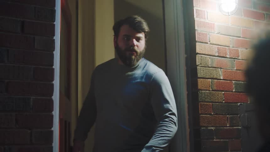 A man conversing with a male visitor at his home entrance at night
