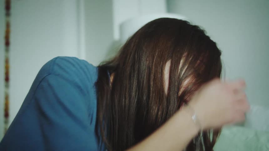 A woman with long brown hair smiling and laughing as she briefly tucks her hair behind her ear revealing a small hoop earring and the side of her face in a softly lit casual indoor setting