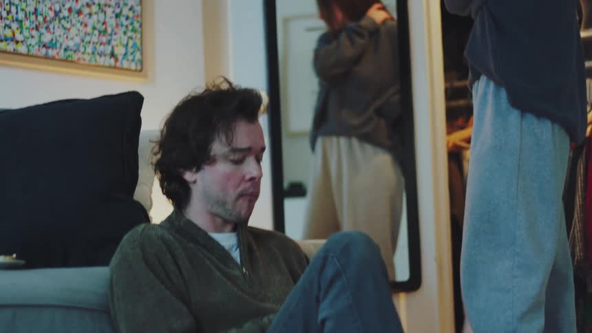 Man is sitting next to a woman who is standing in front of a mirror