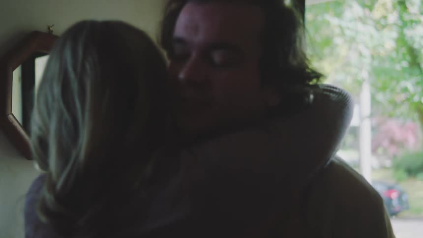 Man arriving at a home with a full backpack puts the bag down to share a hug with a woman