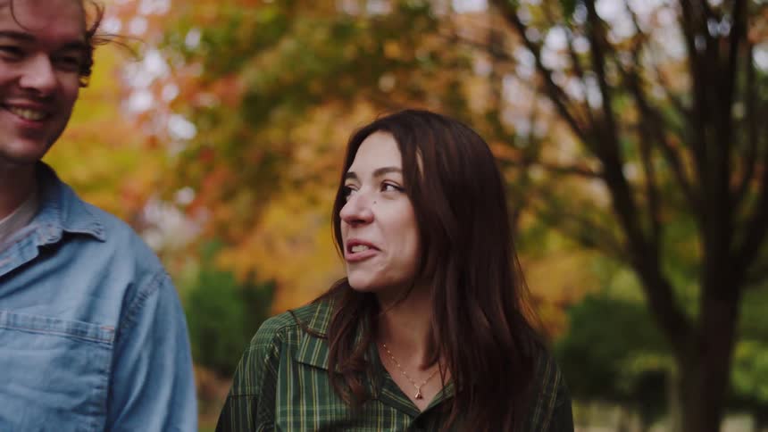 Orange and yellow autumn foliage behind two people in denim and plaid shirts