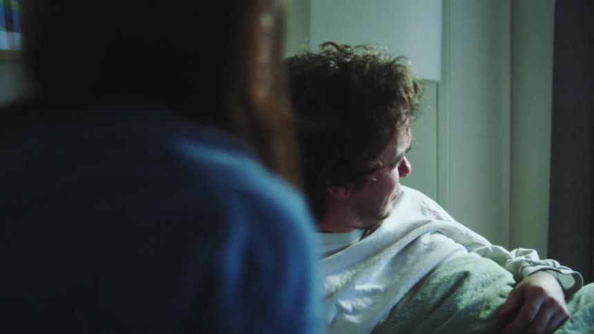 Female person shaking a sleeping young adult man to wake him up while he refuses in a playful manner in a bedroom indoors during day time