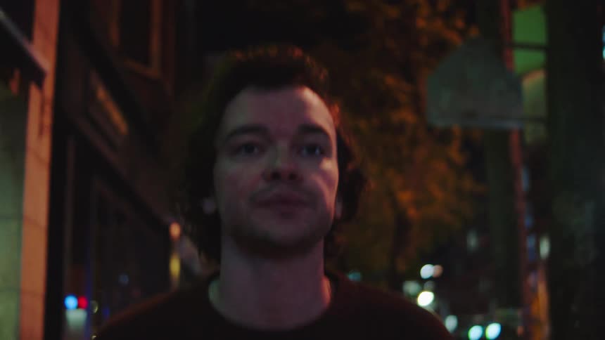 Man walking at night on an urban street lit by streetlights and buildings
