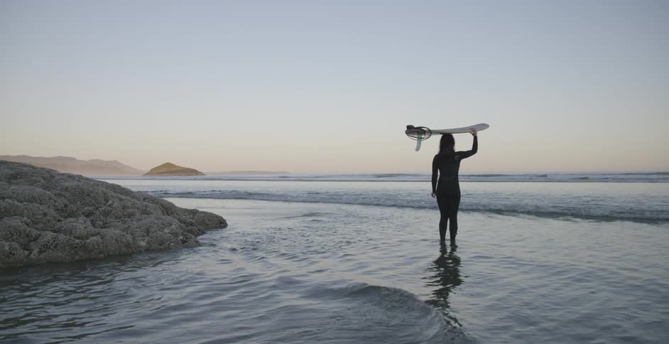 Person holds surfboard on their head standing in the water