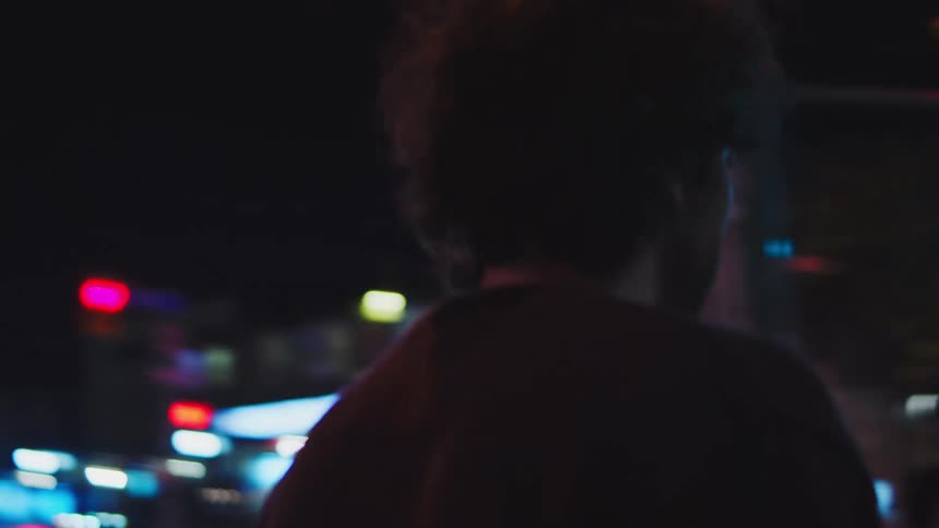 Young adult man walking on the streets downtown on a metropolitan area carrying a mobile phone on his hand and checkingit from time to time outdoors during night time