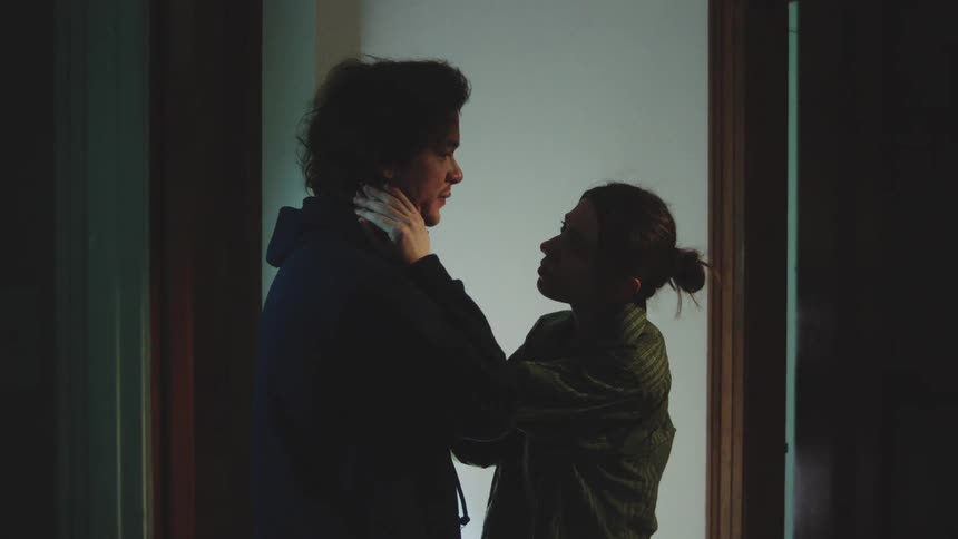 A wife gently comforts her upset husband in a dimly lit room