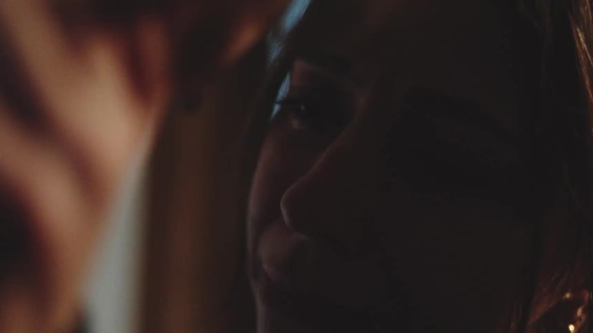 An extreme closeup captures a womans face illuminated by a warm side light as she shows deep distress and is comforted by the touch of a second person during an intimate moment in a dark setting