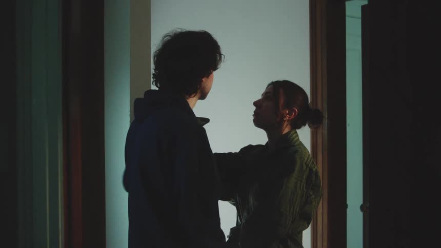 Young adult man and young adult woman holding hands and talking with facial expressions that are sad and nervous indoors during night time