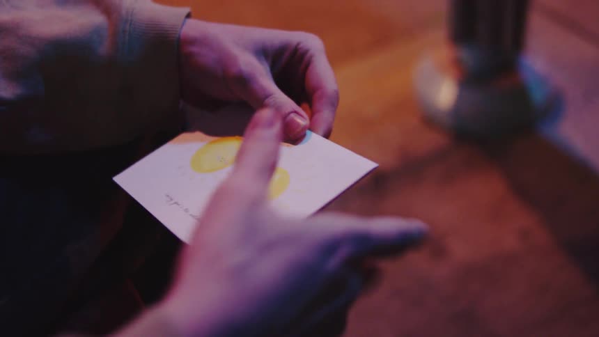 A close view of a mans hands opening a purple envelope and unfolding a white birthday card with handwritten text in a dimly lit setting