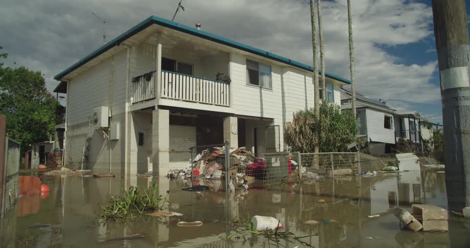 Residential house partially submerged by flood with debris piled at the entrance