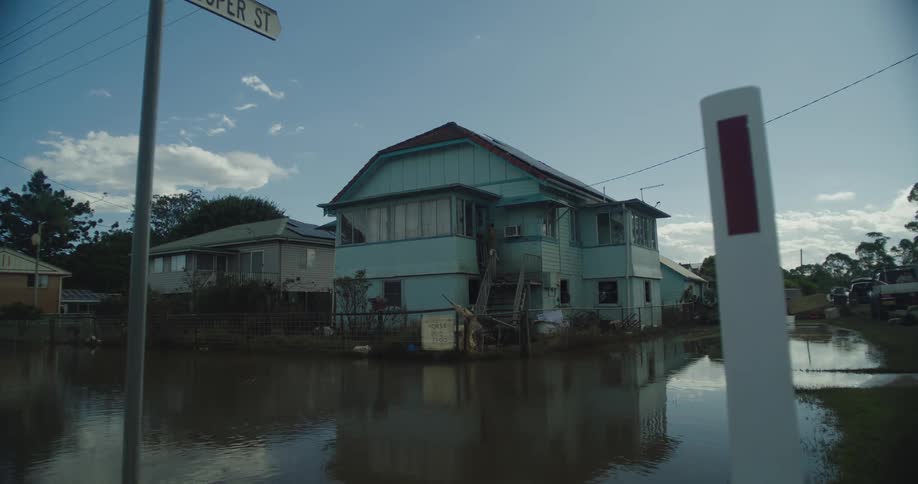 A flooded street with houses submerged in water reflecting the sky and surroundings in the murky surface
