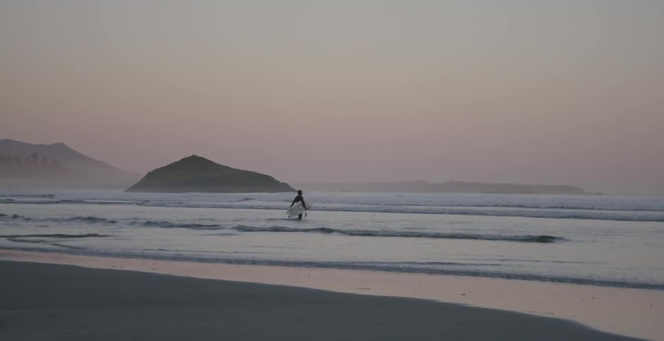 Person carrying a surfboard walking in water