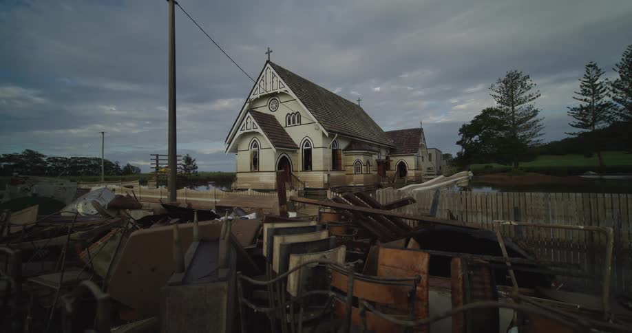 A flooded church stands surrounded by debris under a cloudy overcast sky