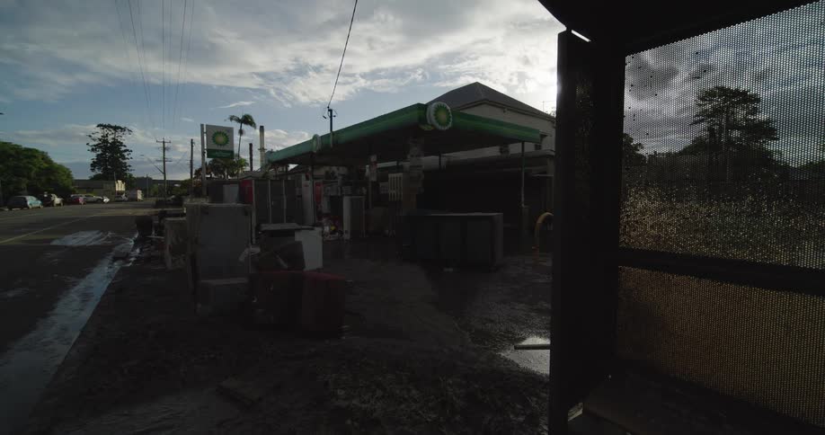 Bp station with green canopy beside bus shelter in area with muddy ground and distant vehicles