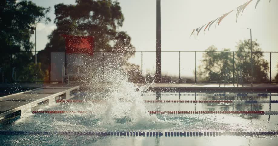 Woman stands at the edge of the swimming pool and dives into the water