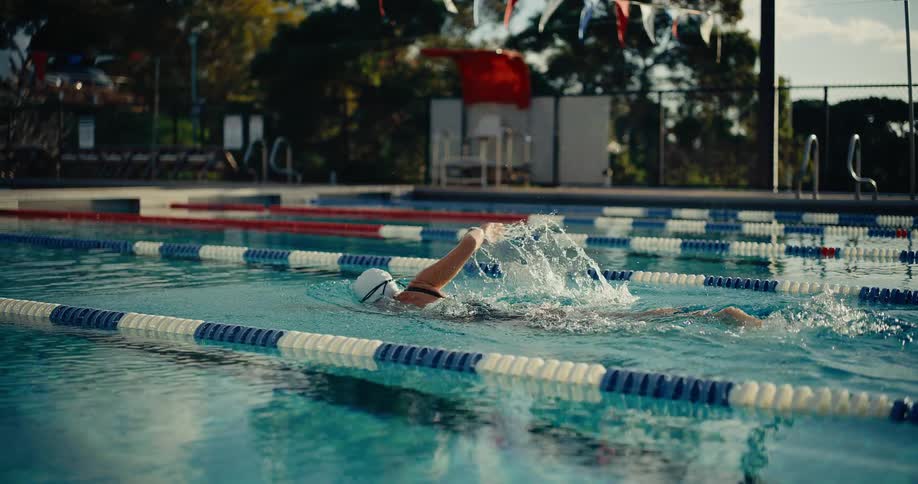 Woman swims in a lane in an outdoor swimming pool on a cloudy summer day