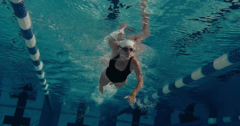 Swimmer in black swimsuit performs freestyle stroke underwater in pool with striped lane dividers