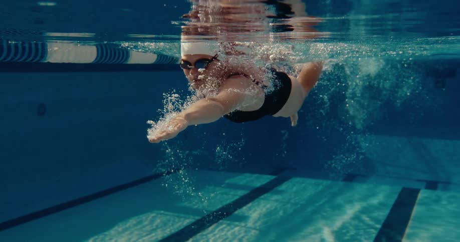 Swimmer in white cap and goggles performs freestyle stroke beneath turbulent water in lanemarked pool