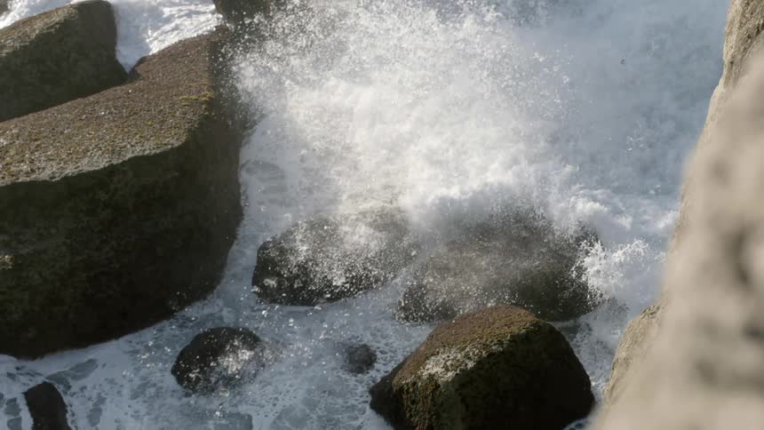 A waves crashes into some rocks at the base of a cliff