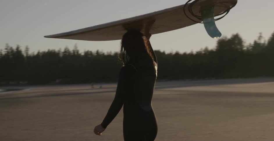 A woman walks on the beach with a surfboard